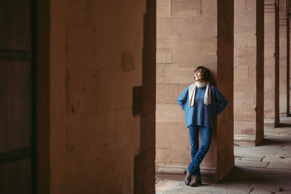 Die Historikerin Annette Kehnel steht an einem Säuleneingang an einem alten Gebäude und lächelt