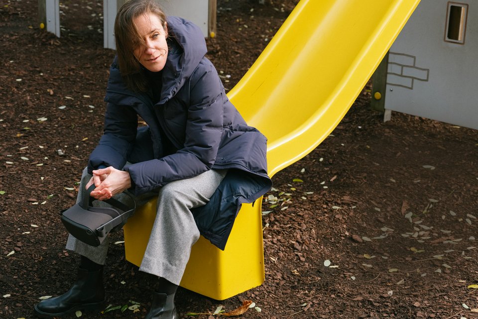Die Psychologin Anna Felnhofer sitzt mit dicker Jacke, die Arme auf die Knie gestützt und die Hände gefaltet, am Ende einer gelben Kinderrutsche und schaut dabei lächelnd in die Ferne