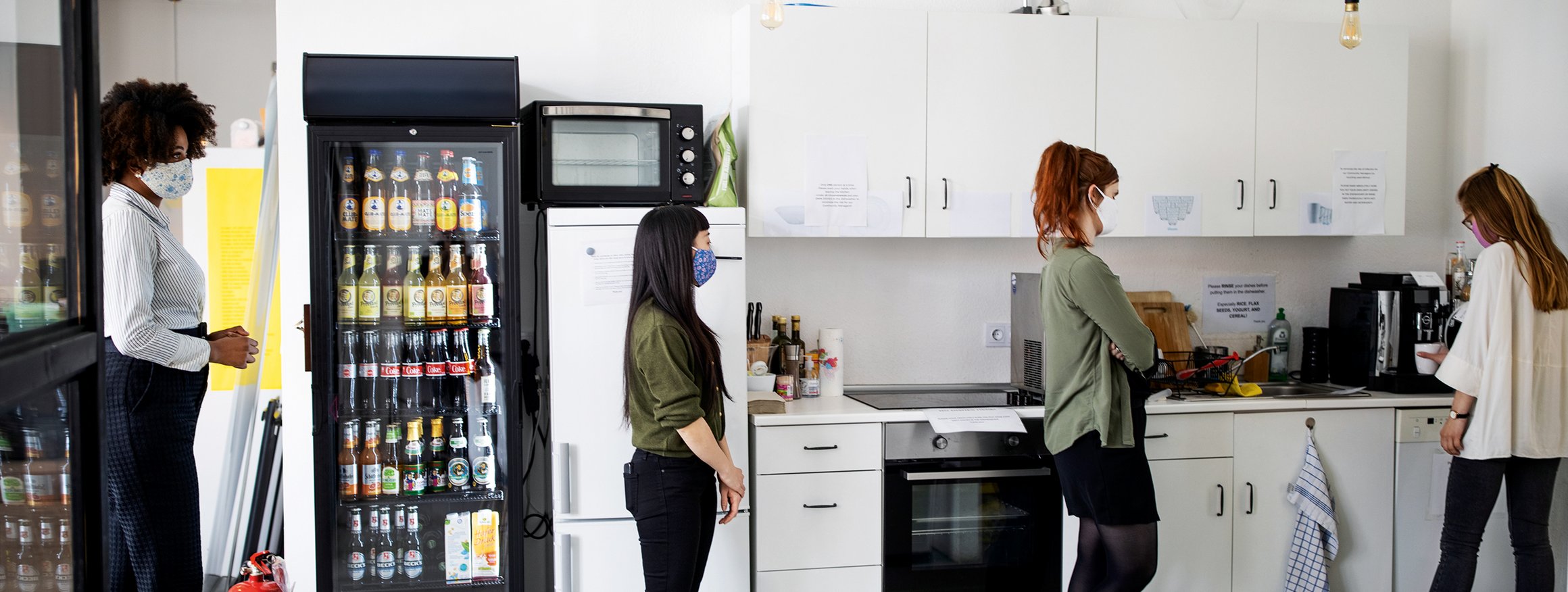 Eine Frau steht in der Büroküche und bedient den Kaffeeautomaten, während hinter ihr zwei Kolleginnen warten, bis sie dran sind