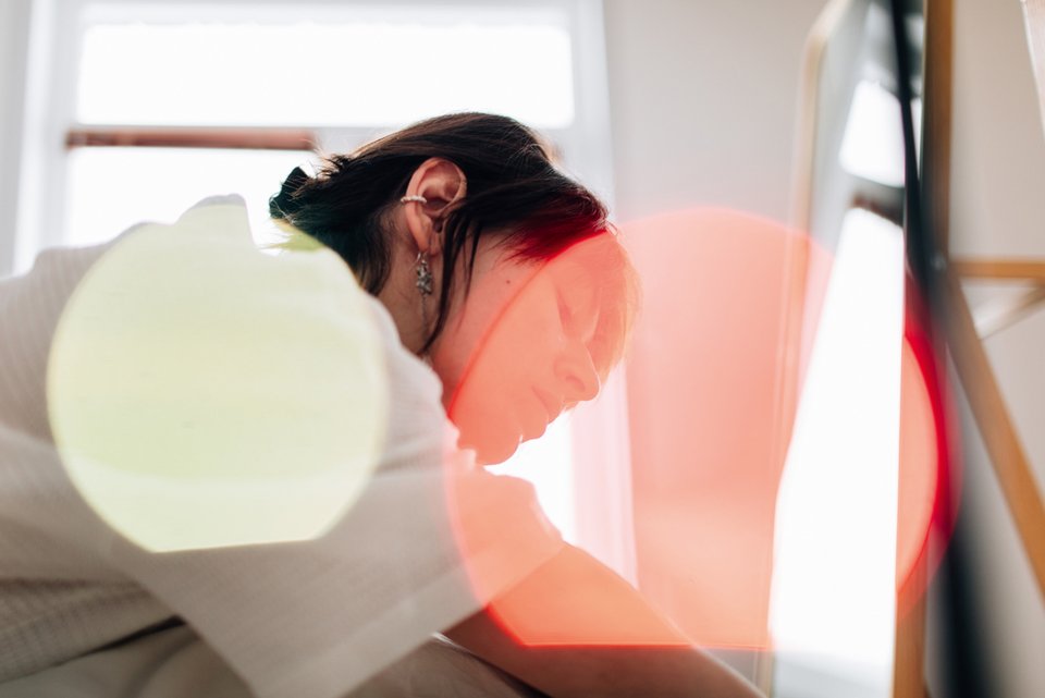 Eine Frau beugt sich nachdenklich vor einem Fenster, während die Sonnenstrahlen ein Lichtspiel um sie herum abzeichnen