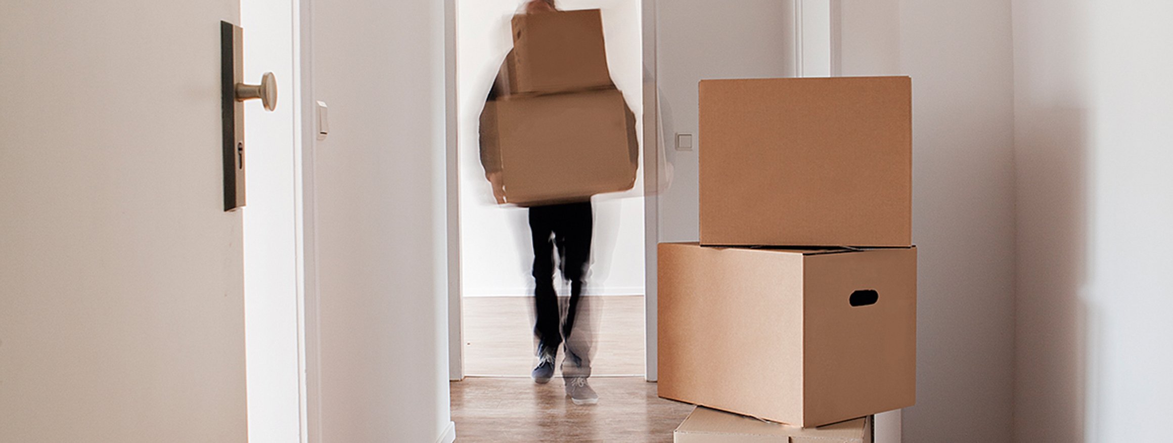 Eine Person zieht um und trägt Umzugskartons in eine leere Wohnung