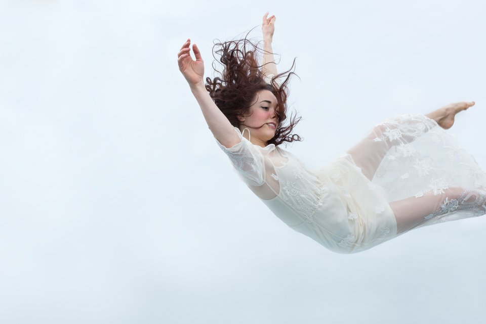 Das Foto zeigt eine Frau in weißem Kleid, die in der Luft schwebt 