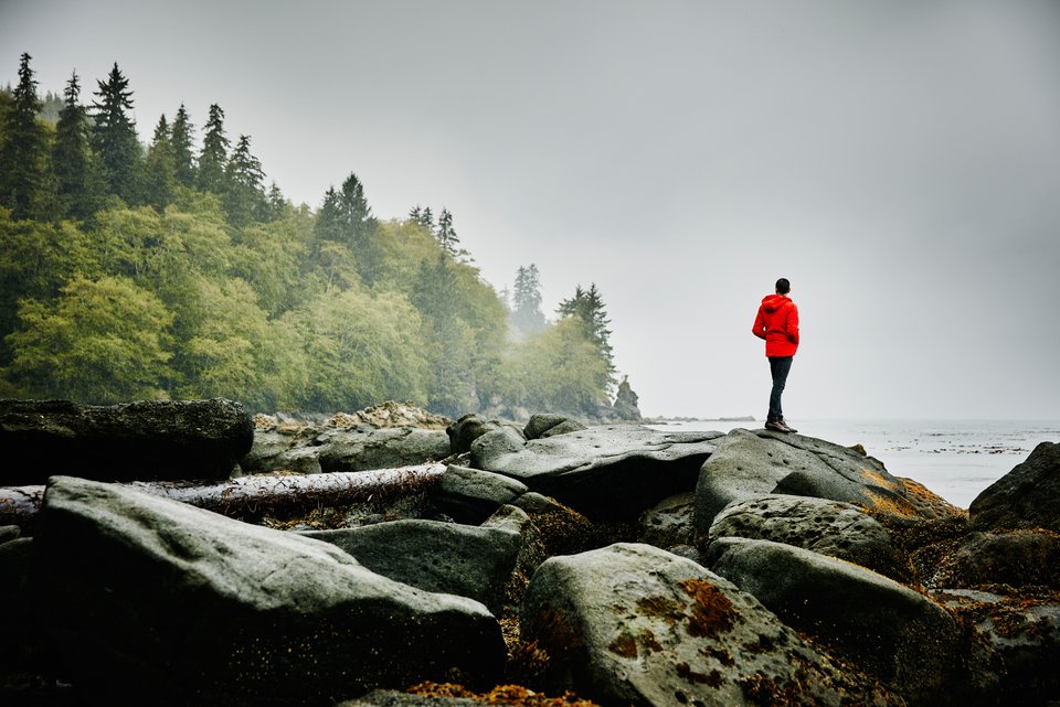 Ein Mann im roten Anorak steht allein auf einem Felsen am Meer