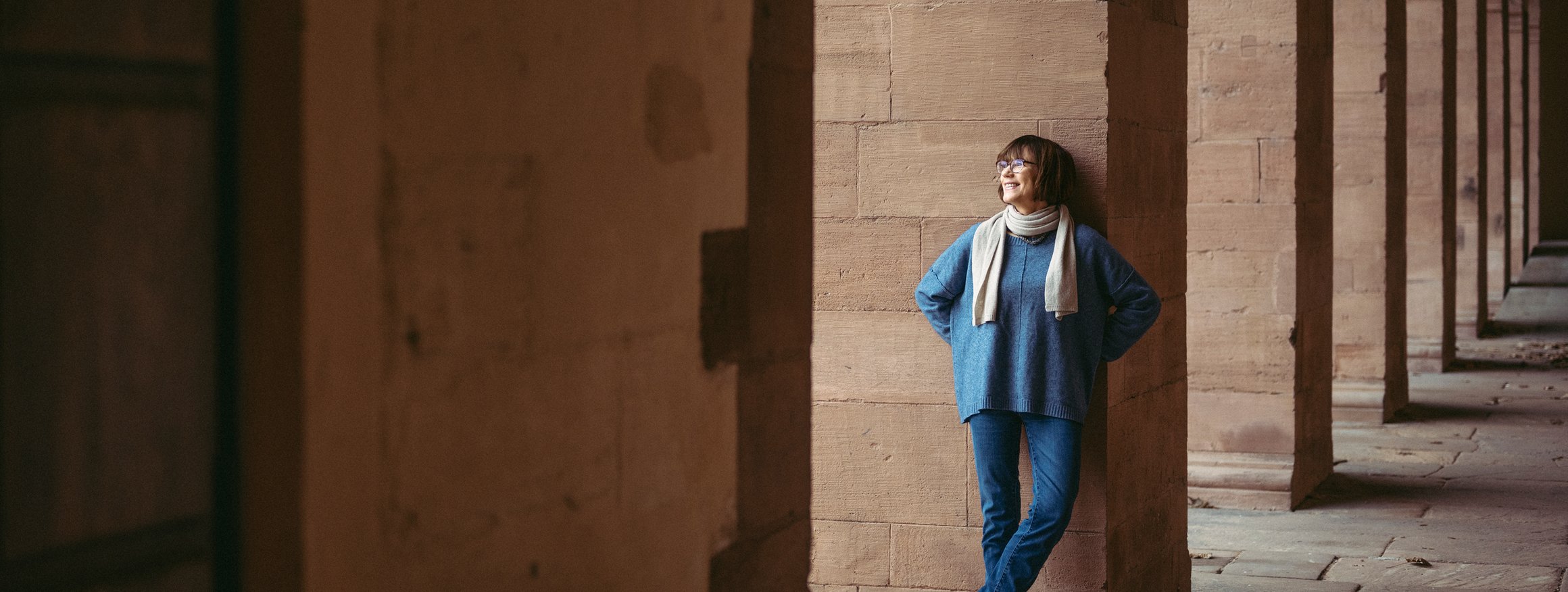 Die Historikerin Annette Kehnel steht an einem Säuleneingang an einem alten Gebäude und lächelt