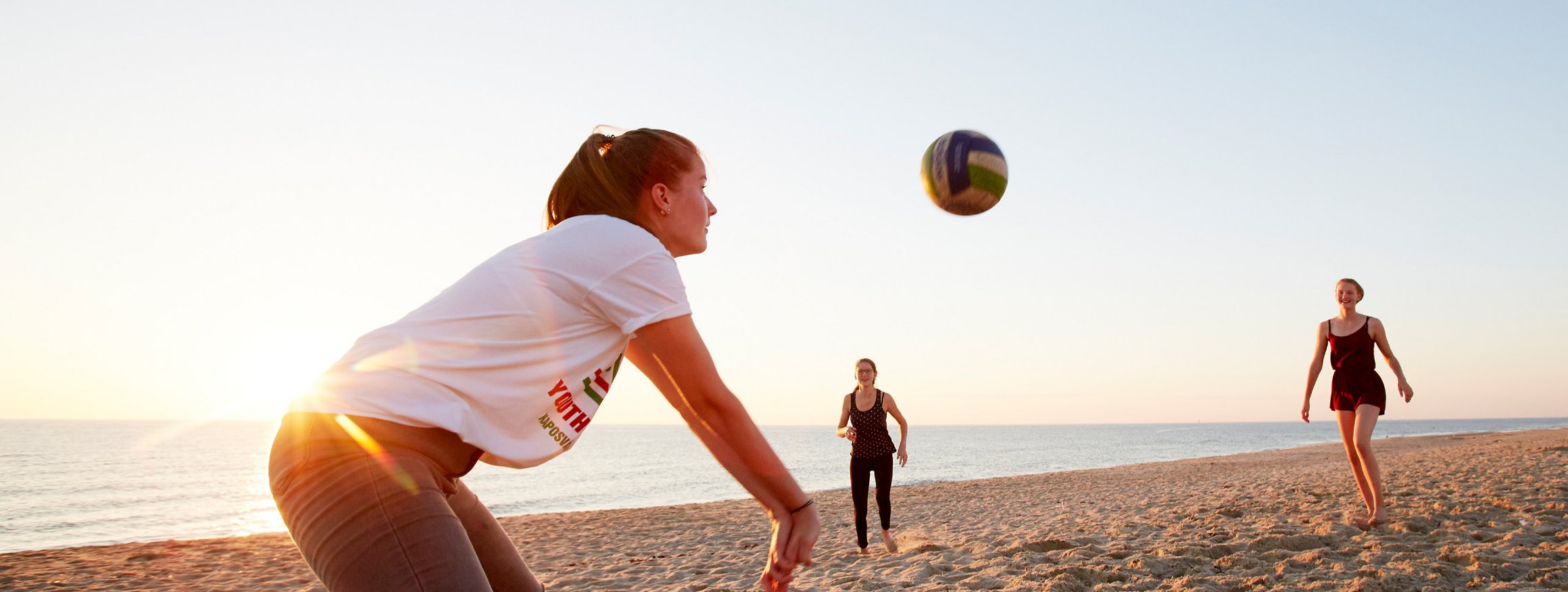 Drei junge Frauen spielen an einem Strand Beachvolleyball