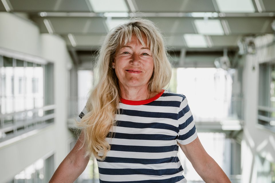 Die Stressforscherin Ulrike Ehlert steht an einem Geländer im Treppenhaus eines modernen Gebäudes und lächelt