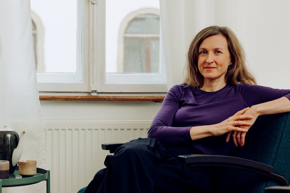 Die Therapeutin Angelika Eck sitzt ruhig lächelnd auf einem Sessel in ihrer Karlsruher Praxis, neben sich ein Tisch mit einer Teekanne, Tassen und einem Glas
