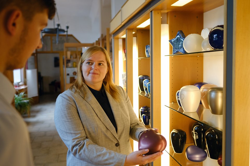Foto zeigt eine Bestatterin, die einem Kunden eine Urne präsentiert