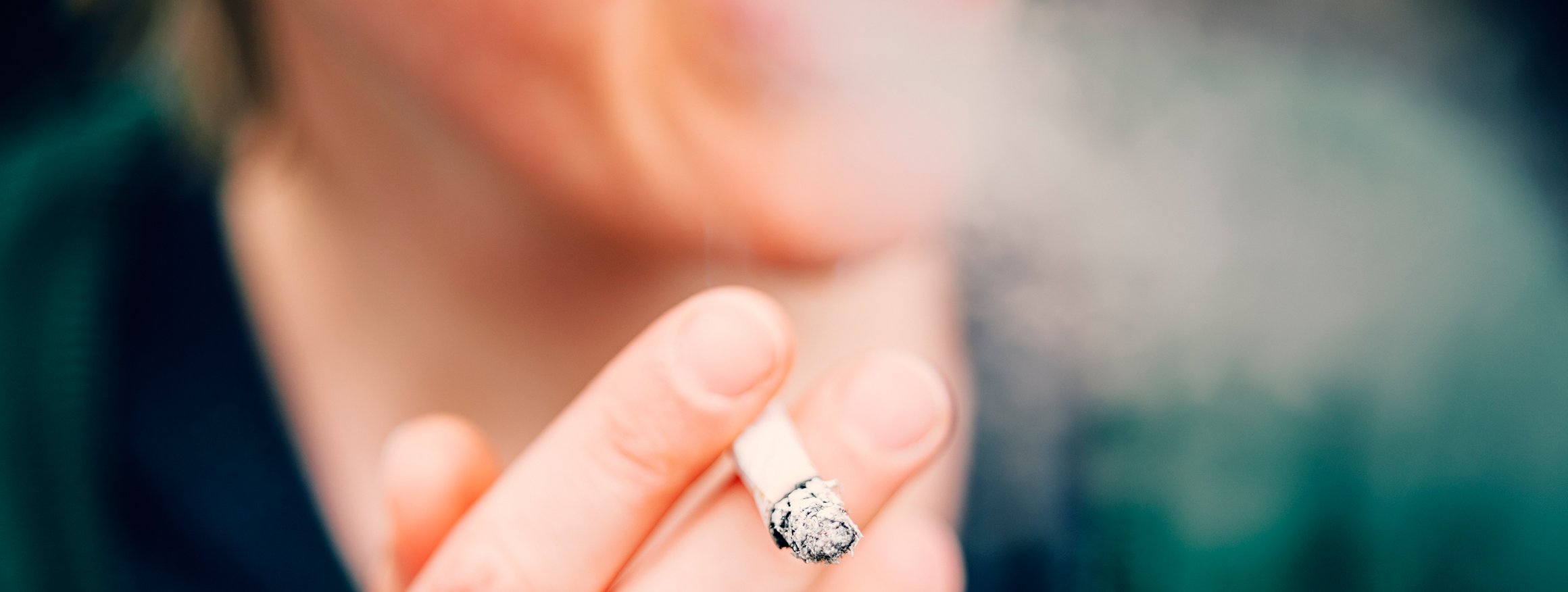 Ein Mann hält eine Zigarette in der Hand und bläst den Rauch heraus