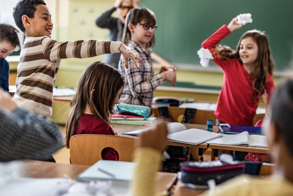 Kinder im Klassenraum werfen ausgelassen mit Papierbällen