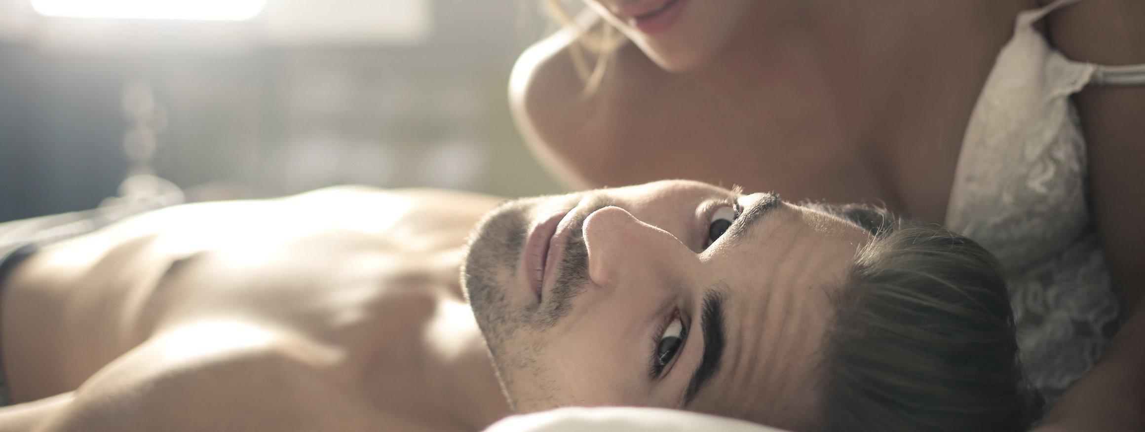 Ein junger Mann ist mit einer Frau im Bett und schaut dabei geheimnisvoll