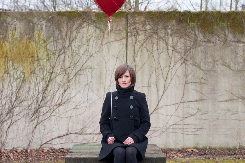 Foto zeigt eine Frau mit einem roten Luftballon in der Hand 