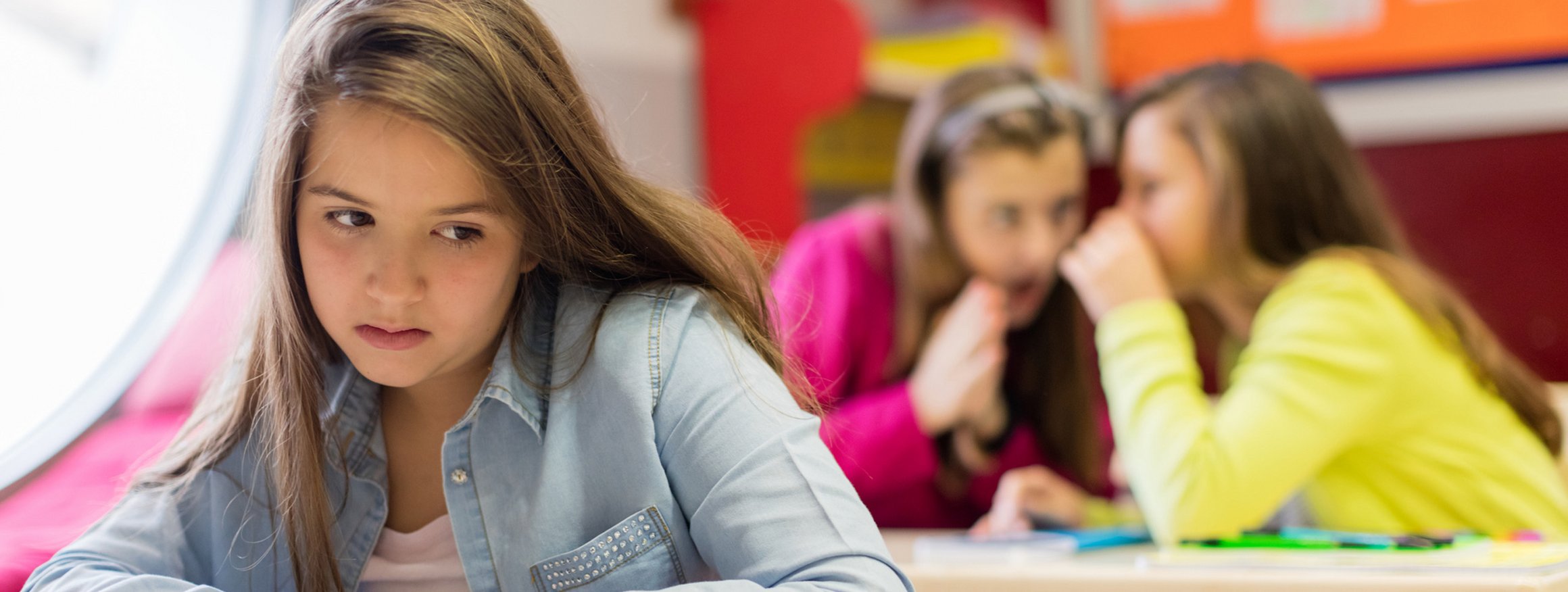 Ein Mädchen schaut unglücklich und fühlt sich ausgeschlossen, weil Klassenkameradinnen in der Schule hinter ihrem Rücken über sie reden.