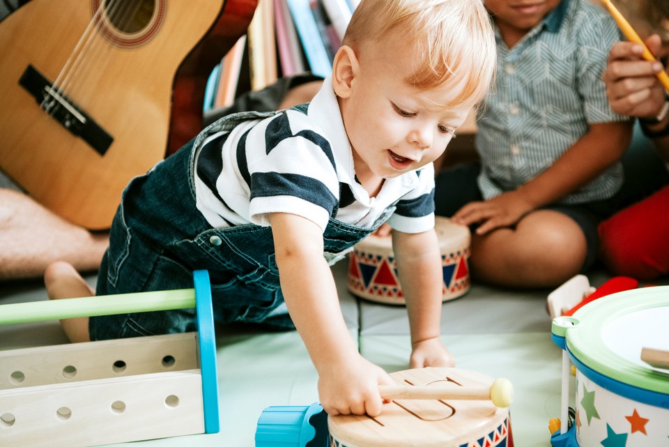 Ein Kleinkind sitzt inmitten einer Kindergruppe und trommelt auf einem Holzinstrument