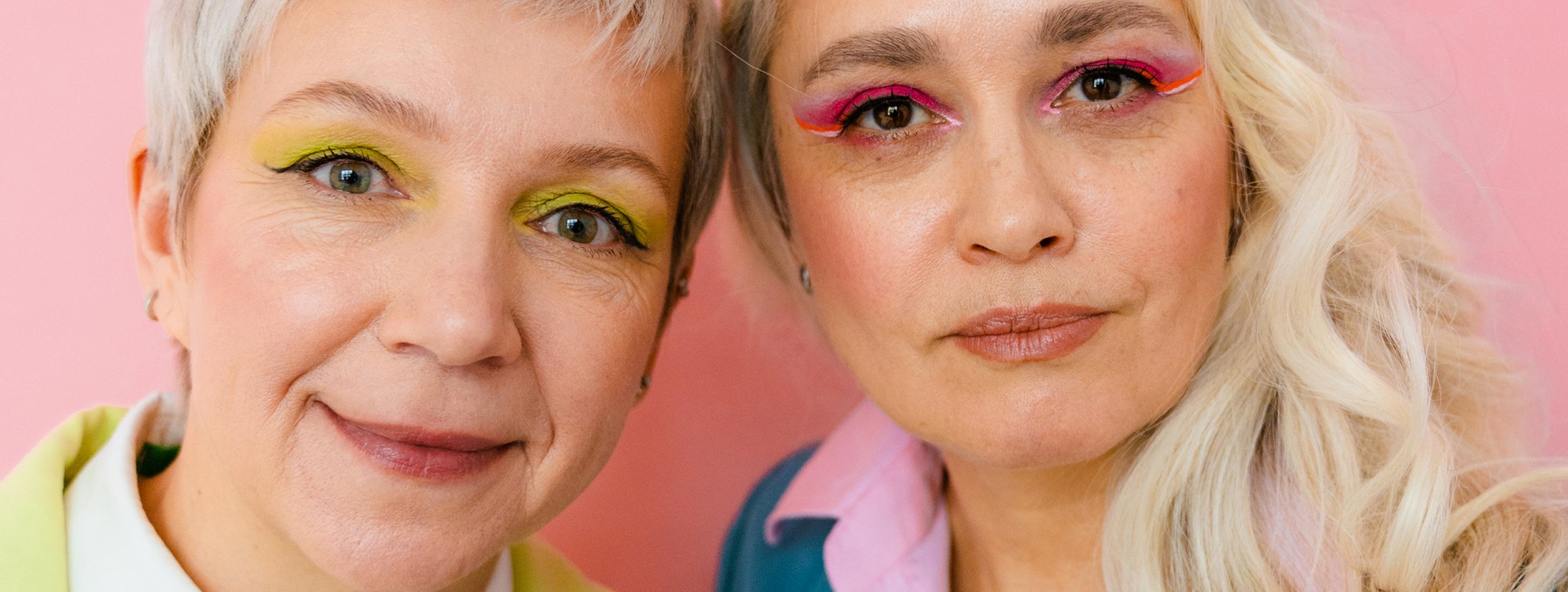 Zwei ältere Frauen in farbenfroher Kleidung und farbigen Augen-Makup, stehen nah beieinander