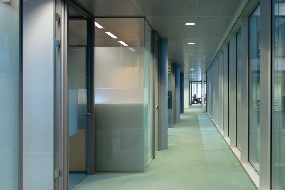 Ein sehr langer und grauer Flur, an dessen Ende ein Angestellter in einem Büro sitzt 