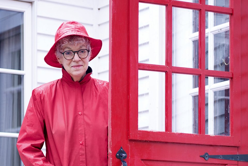 Die renommierte Psychologin und Princeton-Professorin Susan Fiske, steht im roten Regenmantel und rotem Hut an ihrer roten Eingangstür
