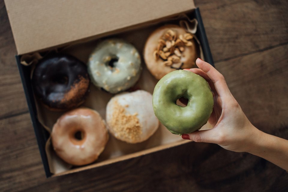 Eine Frauenhand greift in eine Donutschachtel und holt sich einem Donut mit grüner Glasur heraus