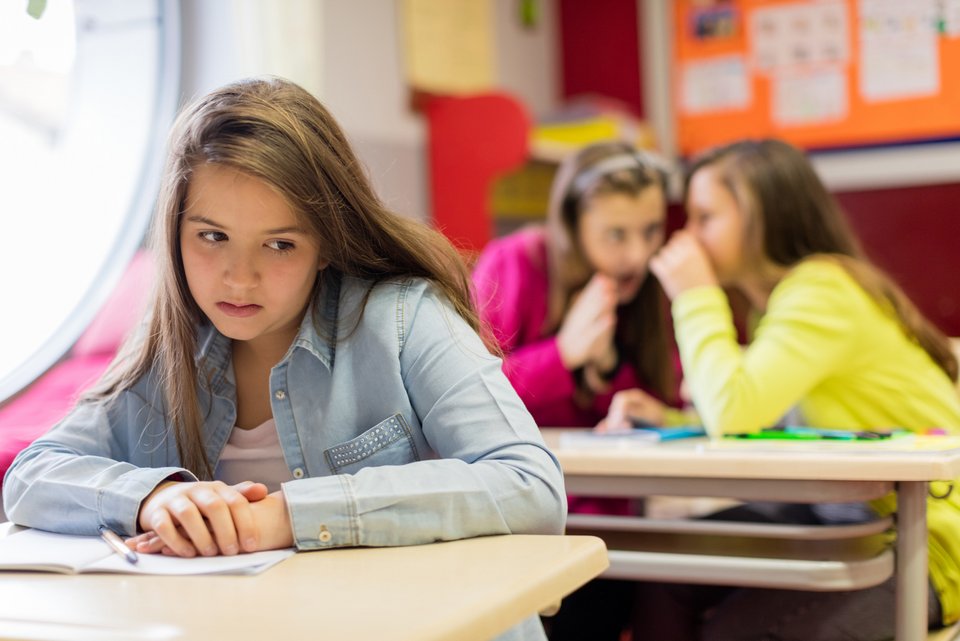 Ein Mädchen schaut unglücklich und fühlt sich ausgeschlossen, weil Klassenkameradinnen in der Schule hinter ihrem Rücken über sie reden.