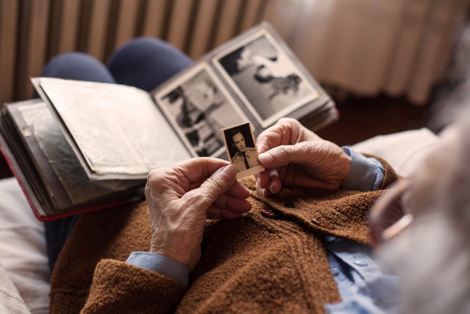 Eine alte Frau hält ein altes schwarz-weiß Foto in der Hand und denkt an einen toten geliebten Menschen 