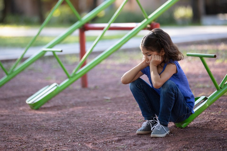 Ein kleines Mädchen sitzt allein und traurig auf einer Wippe auf einem Spielplatz