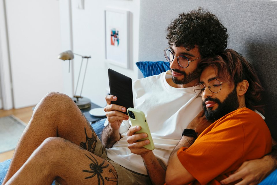 Ein Paar liegt eng beieinander, während jeweils beide ein Smartphone in der Hand halten und darauf schauen