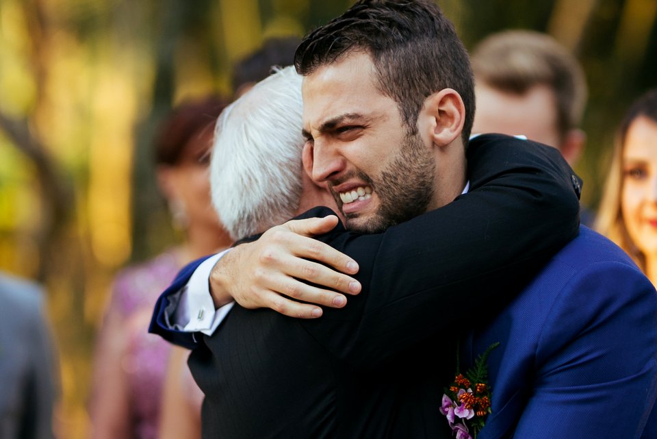 Ein junger Bräutigam wird auf seiner Hochzeit von einem älteren Mann umarmt und weint dabei vor Freude