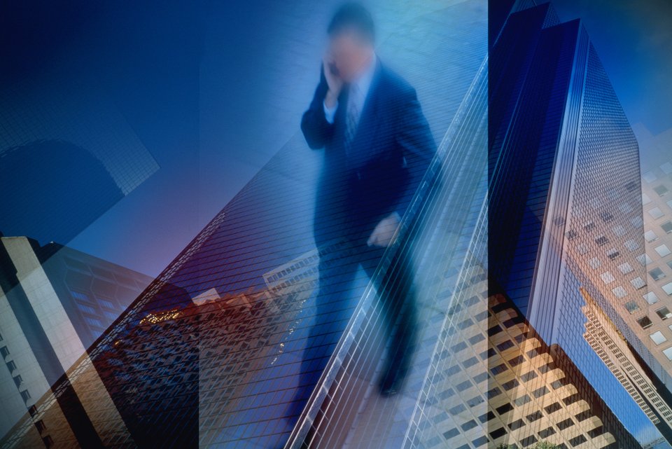 Ein Businessmann mit Anzug, Krawatte und Smartphone am Ohr läuft durch eine Skyline im Bankenviertel
