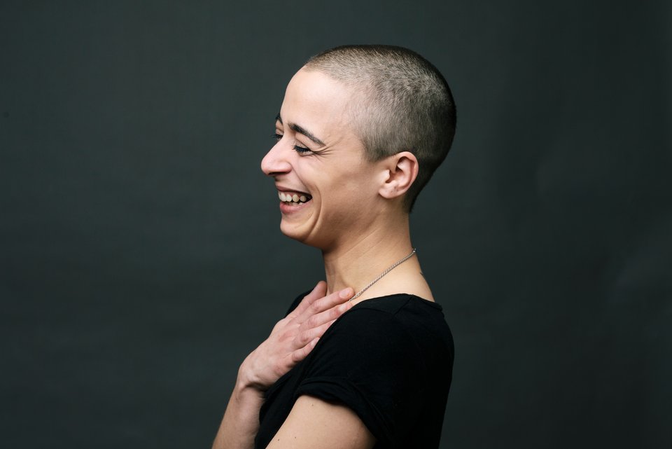Das Foto zeigt eine lachende Frau mit rasiertem Kopf.