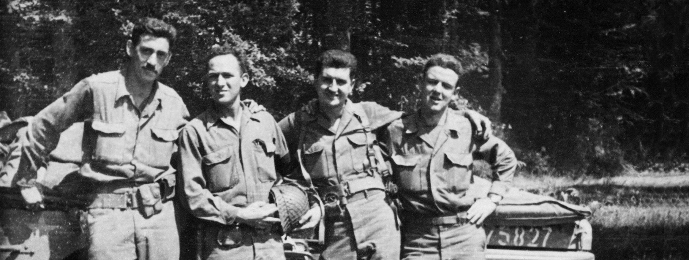 Der Schriftsteller J.D. Salinger steht während des 2. Weltkrieges gemeinsam mit seinen Kameraden vor einem Militärfahrzeug