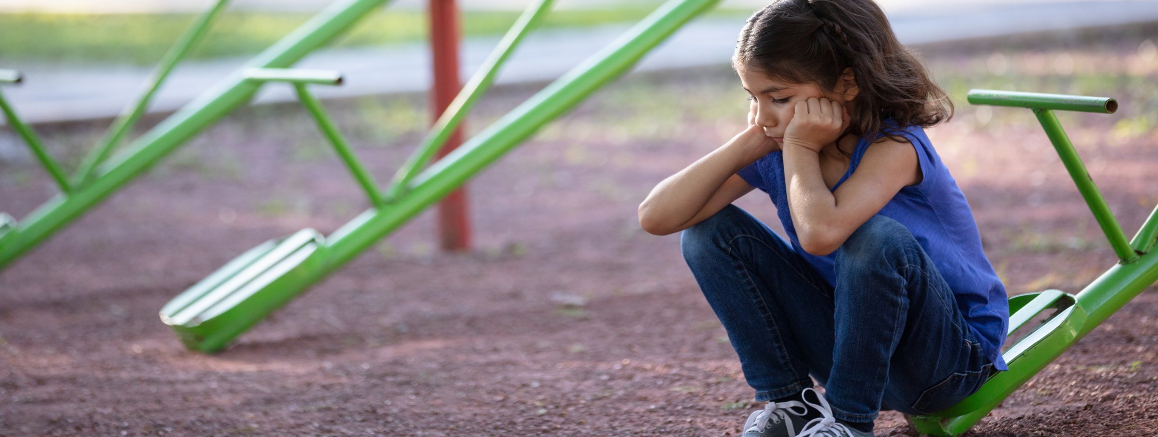 Ein kleines Mädchen sitzt allein und traurig auf einer Wippe auf einem Spielplatz