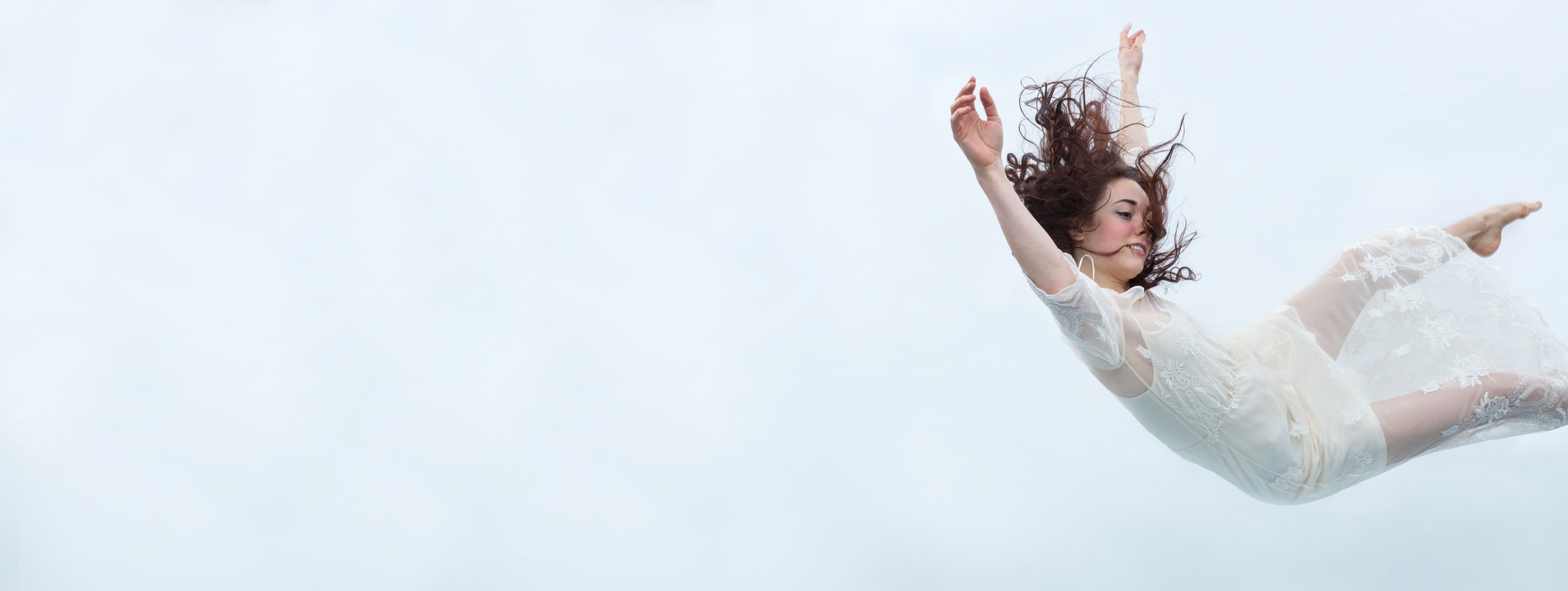 Das Foto zeigt eine Frau in weißem Kleid, die in der Luft schwebt.