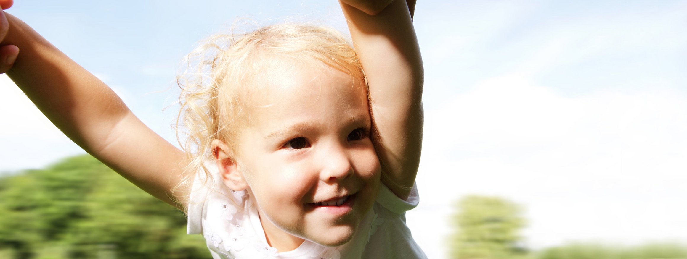 Ein kleines, blondes Mädchen wird sicher von seinen Eltern an den Händen in der Luft im Kreis gedreht