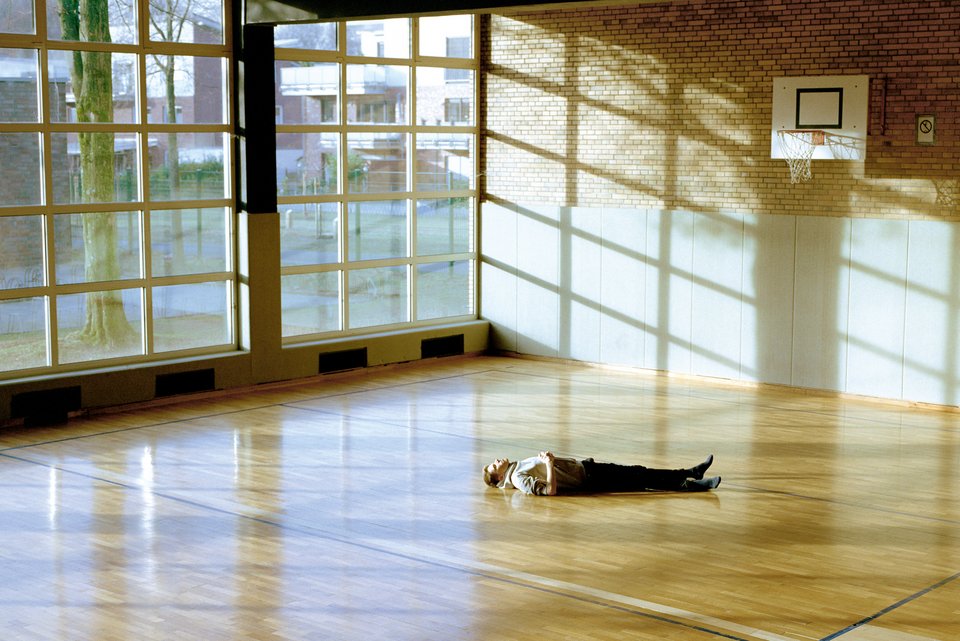 Ein junger Mann liegt in einer Sporthalle traurig auf dem Boden und blickt an die Decke.