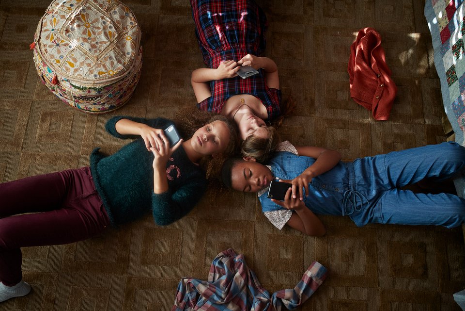 Das Foto zeigt, drei Kinder, die auf dem Boden eines Kinderzimmers liegen. Alle halten ihre Smartphones in den Händen und tippen darauf.