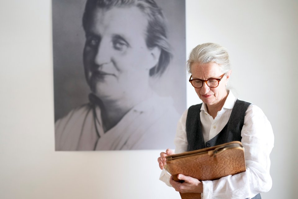 Die Schriftstellerin Melitta Breznik steht vor einer Wand, an der ein Foto ihrer Großmutter hängt