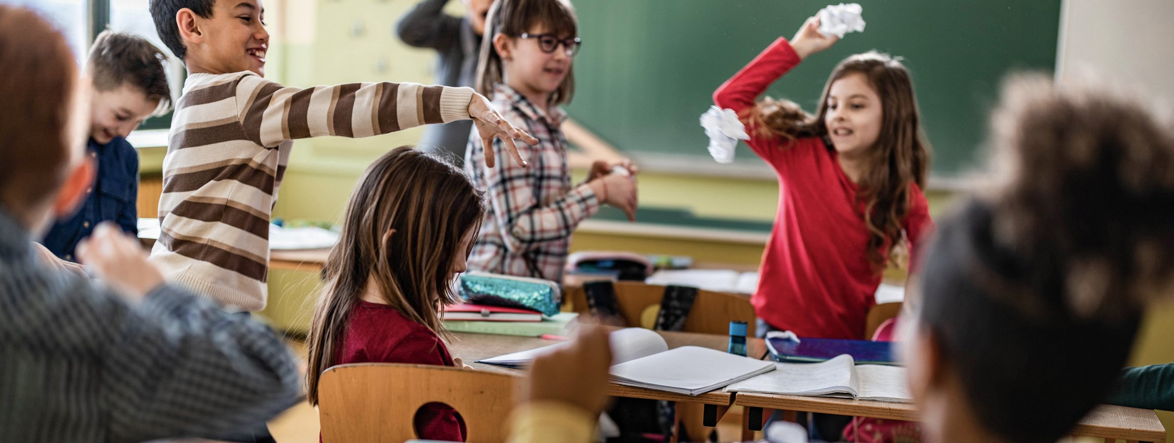 Kinder im Klassenraum werfen ausgelassen mit Papierbällen