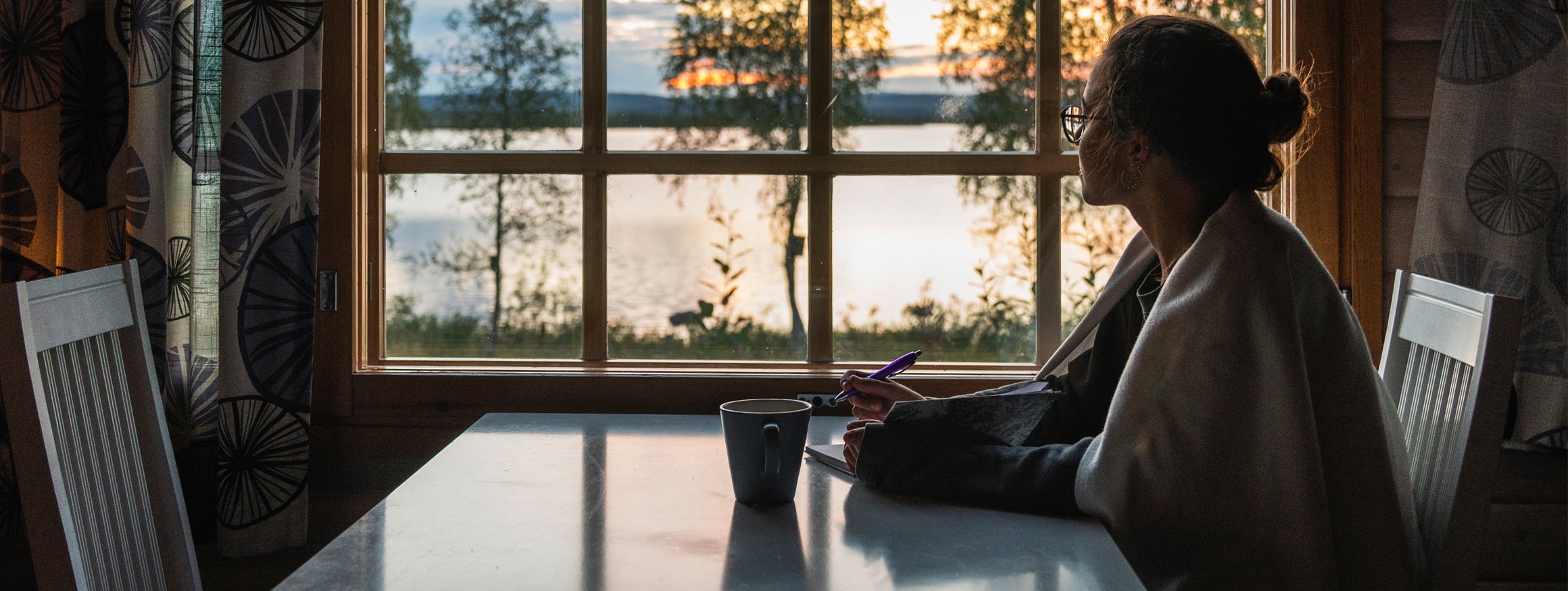 Das Foto zeigt eine Frau, die am Tisch sitzt und in ein Notizbuch schreibt