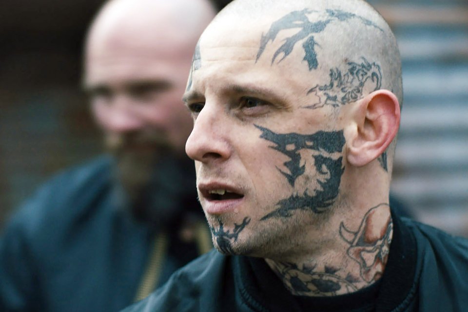Ein Skinhead mit Tattoos im Gesicht schaut aggressiv