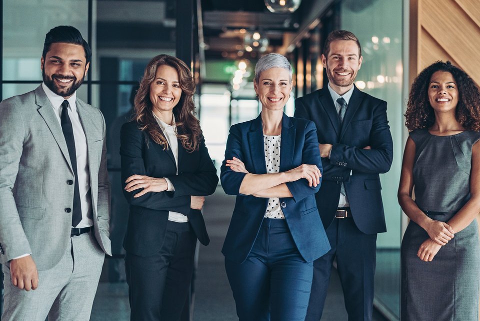 Diverses Team steht in Business-Kleidung in einer Reihe und lächelt gutgelaunt