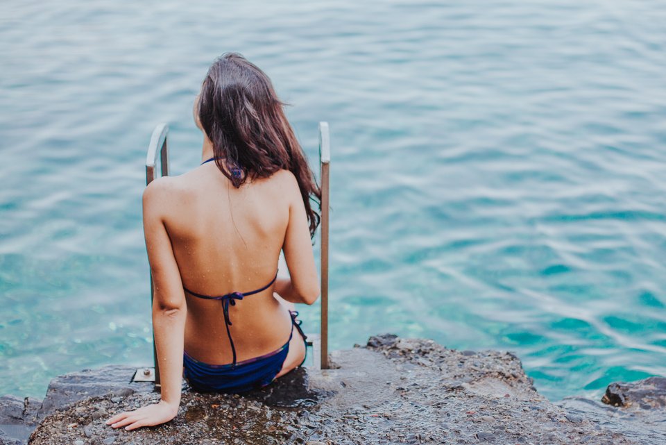 Ein dünnes Mädchen sitzt im Bikini auf einem Felsen am Meer