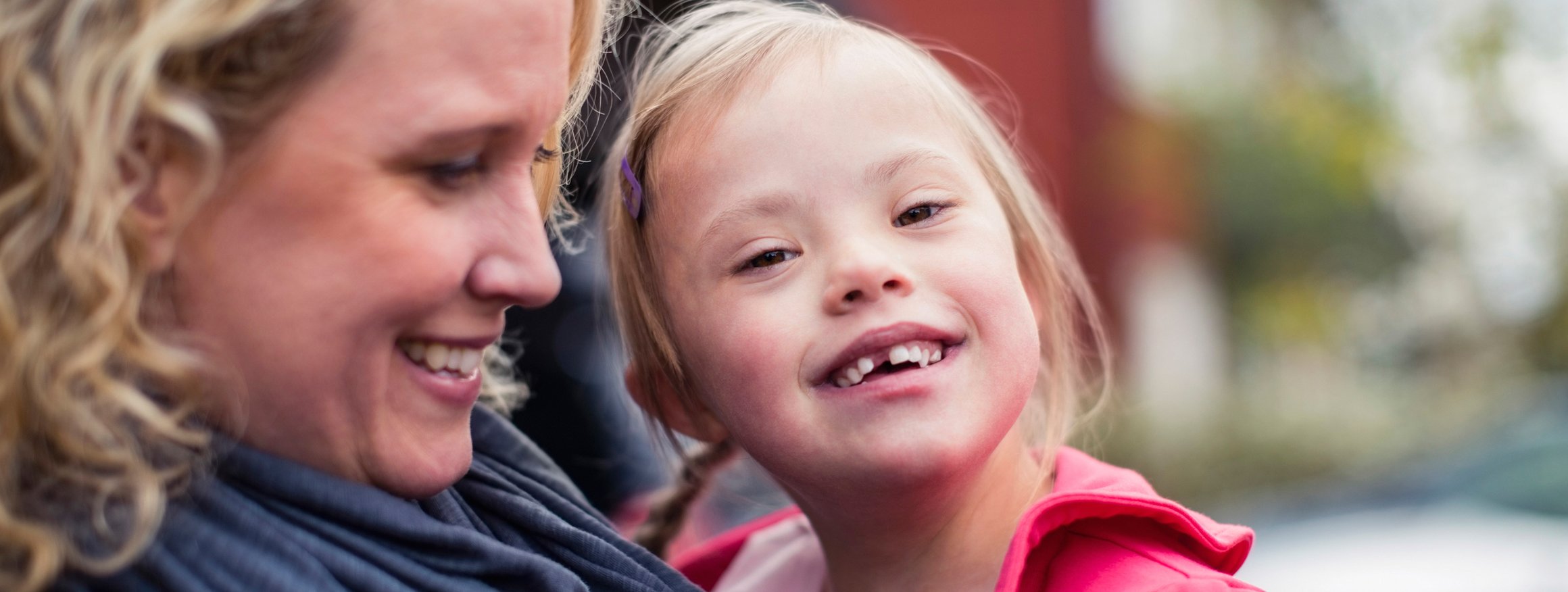 Eine Mutter hält lächelnd ihr fröhliches Kind im Arm, dass das Downsyndrom hat