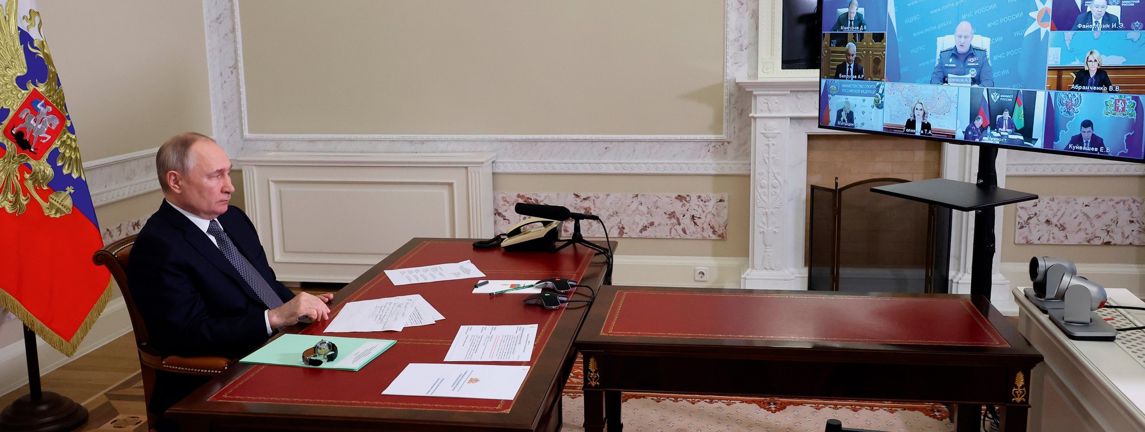 Wladimir Putin sitzt an seinem Regierungstisch  mit Papieren vor der russischen Fahne